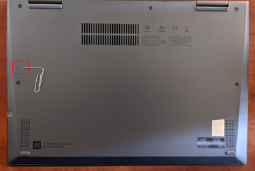 The bottom of a laptop with a red highlighted over a paperclip and the hole